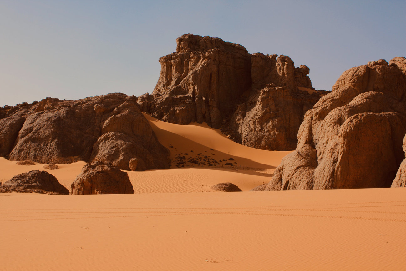 Large rock formations rise from smooth sand in a desert landscape.