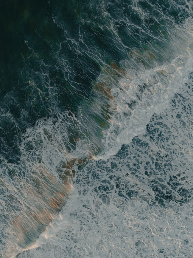 Foamy ocean waves spread across the shoreline in an aerial view.