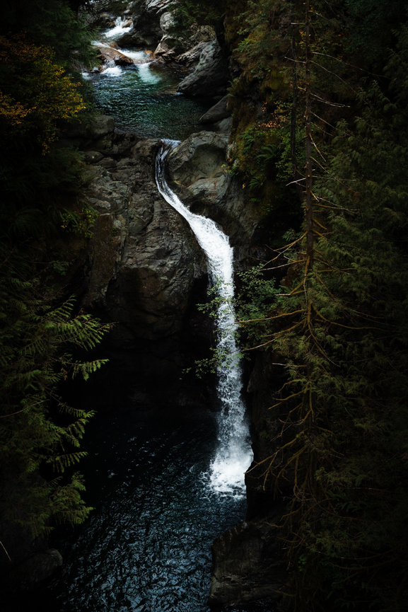 A white waterfall flows through a deep green forest canyon.
